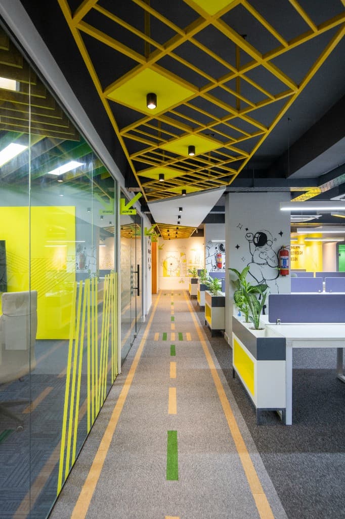 Modern office hall with yellow-accented glass rooms and open workstations